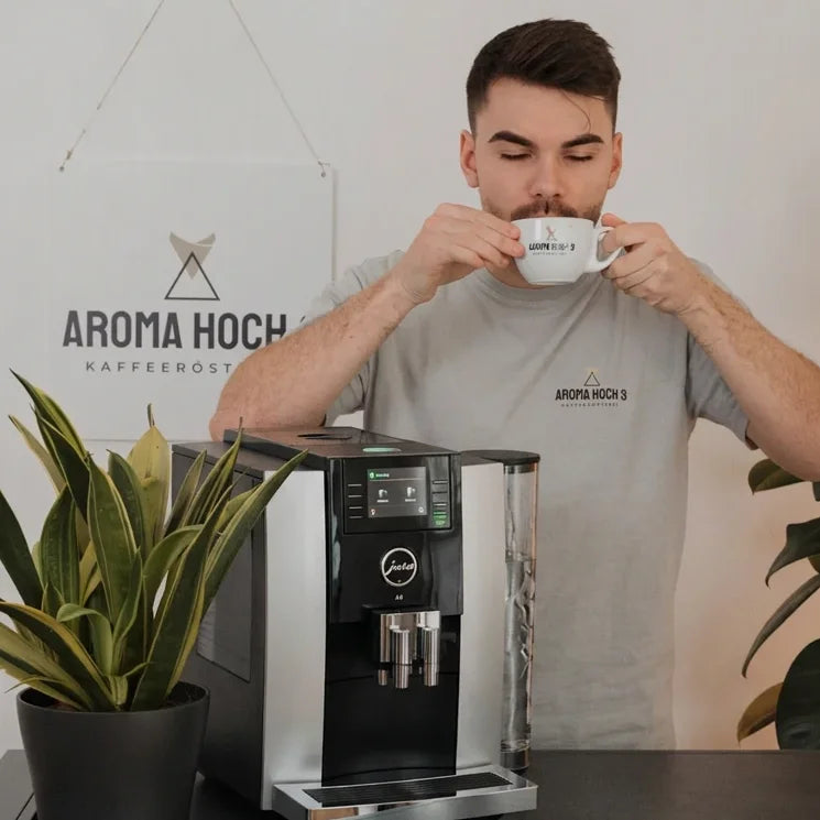 Ferdi trinkt einen Kaffee, vor ihm steht ein Kaffeevollautomat